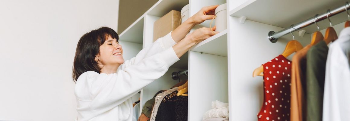 Person räumt eine weiße Box in einen weißen Kleiderschrank ein